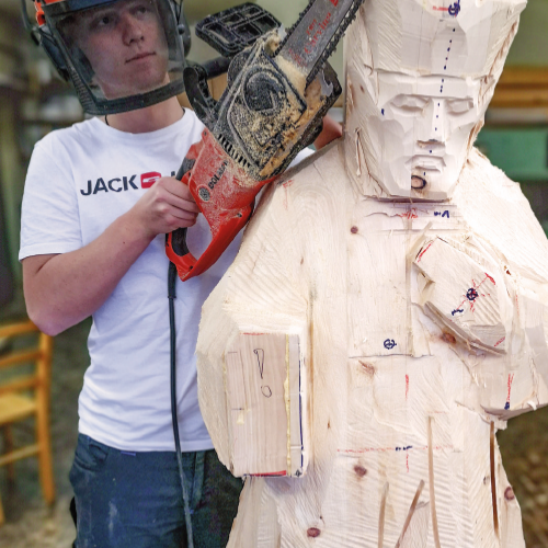 Schüler arbeitet mit Motorsäge an lebensgroßer Skulptur Heiliger Nepomuk