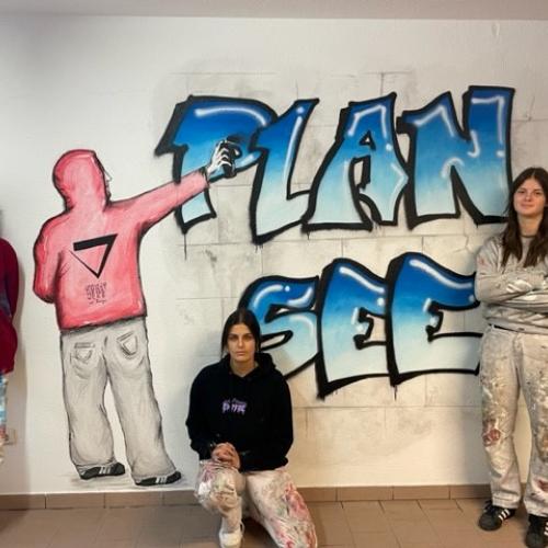 Drei Schülerinnen vor einer gestalteten Wand mit der Plansee