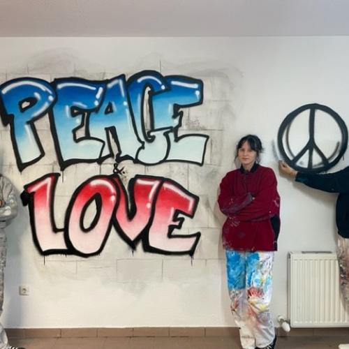 Drei Schülerinnen vor einer gestalteten Wand mit der Aufschrift Peace Love